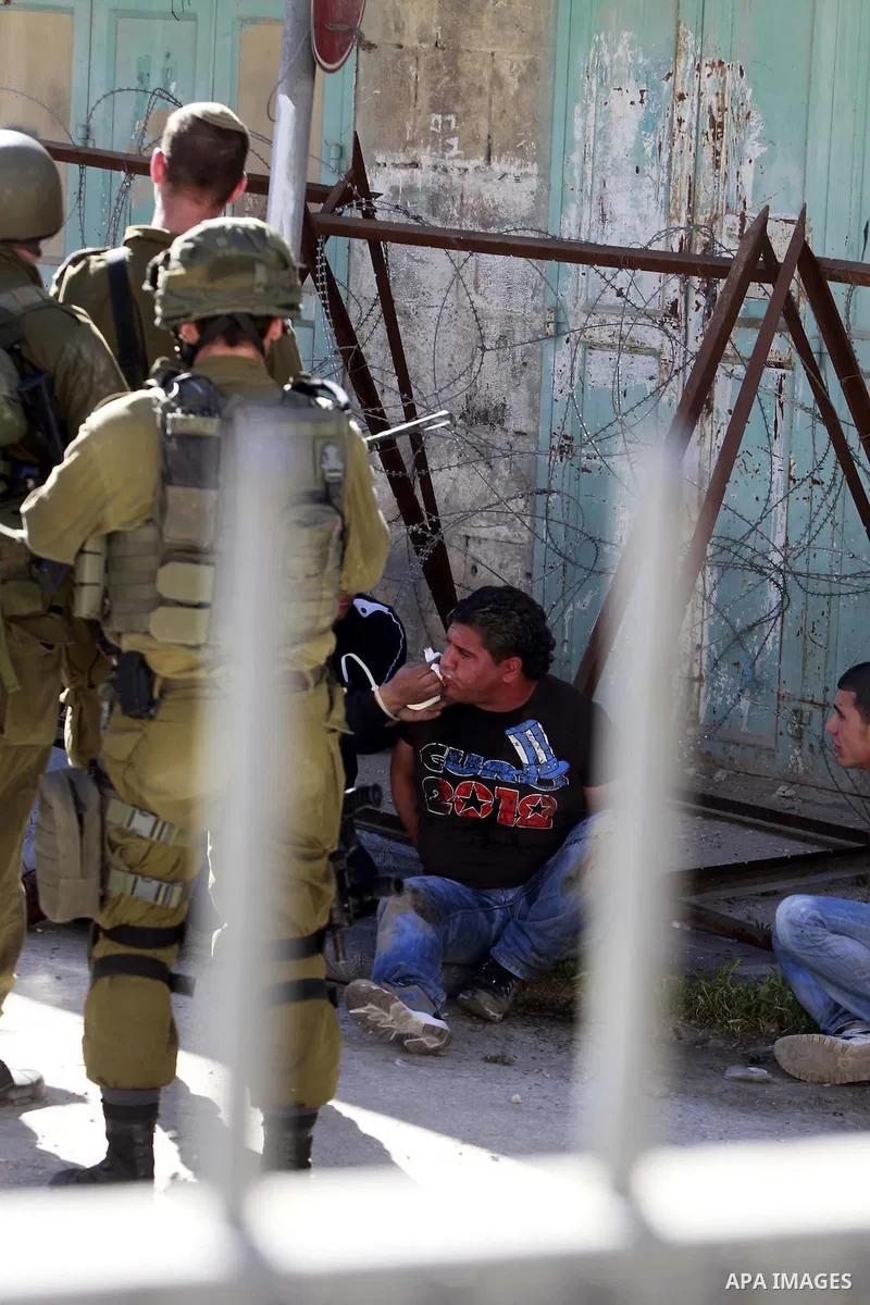 Israeli soldiers guard three Palestinians who were handcuffed with plastic cords after being arrested following clashes between Palestinians and Israeli soldiers in the West Bank city of Hebron, 28 March 2014. Photo by M...