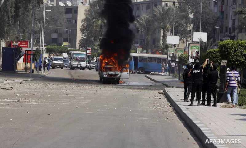 Riot police take their positions in front of a police car set on fire by students of Al-Azhar University during clashes with supporters of the Muslim Brotherhood and deposed President Mohamed Mursi at University's campus...