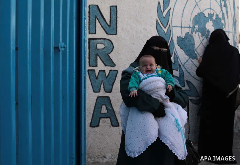 A Palestinian woman carries her son during a protest a the decision made by the United Nations Relief and Works Agency (UNRWA) to reduce food aid delivered to the Gaza Strip in front of the UNRWA headquarters in Gaza Cit...