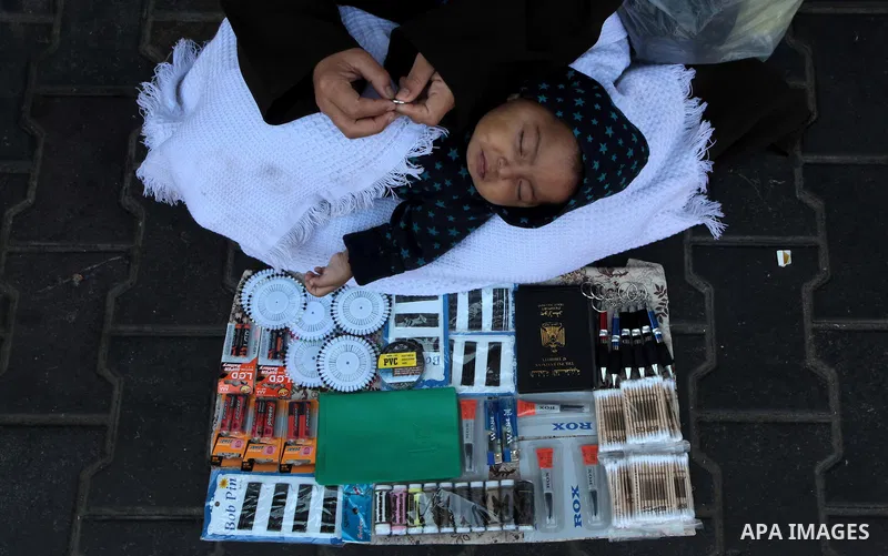 A Palestinian woman holds her baby boy as she sells stuff at a street in Gaza City on April 29, 2014. The Israeli government has begun implementing economic sanctions it had imposed on the Palestinian Authority after app...