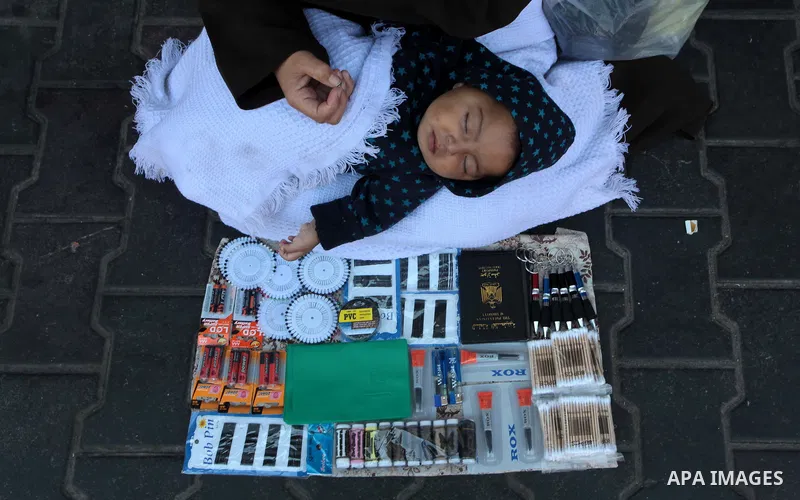 A Palestinian woman holds her baby boy as she sells stuff at a street in Gaza City on April 29, 2014. The Israeli government has begun implementing economic sanctions it had imposed on the Palestinian Authority after app...