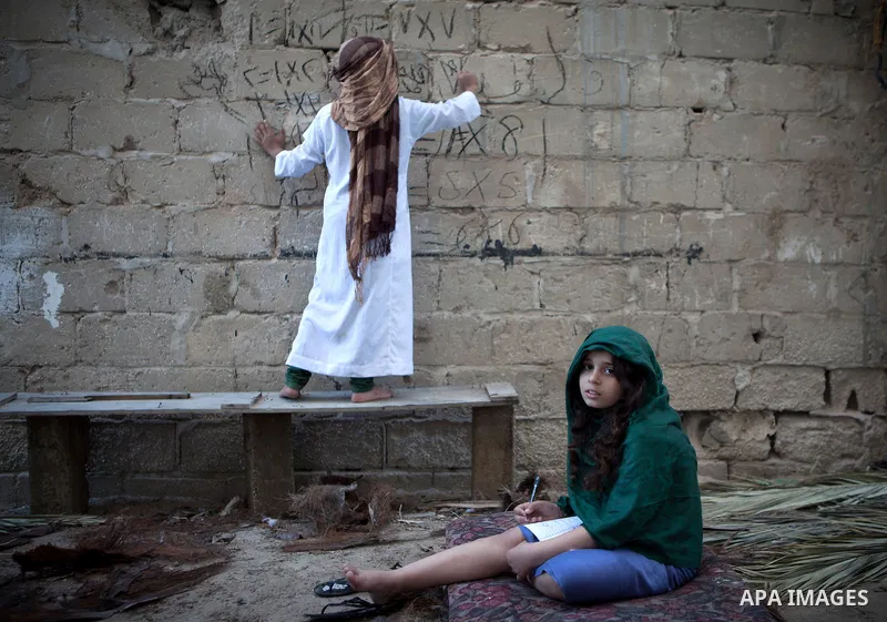 A Palestinian boy writes on a wall as he plays with his sister outside their family's house, in the east of ‎Gaza‬ City near the border with Israel, May 1, 2014. Photo by Ezz Zanoun