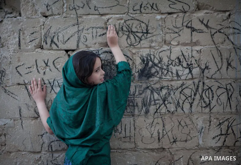A Palestinian girl writes on a wall as she plays outside her family's house, in the east of ‎Gaza‬ City near the border with Israel, May 1, 2014. Photo by Ezz Zanoun