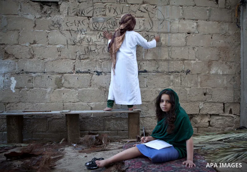 A Palestinian boy writes on a wall as he plays with his sister outside their family's house, in the east of ‎Gaza‬ City near the border with Israel, May 1, 2014. Photo by Ezz Zanoun