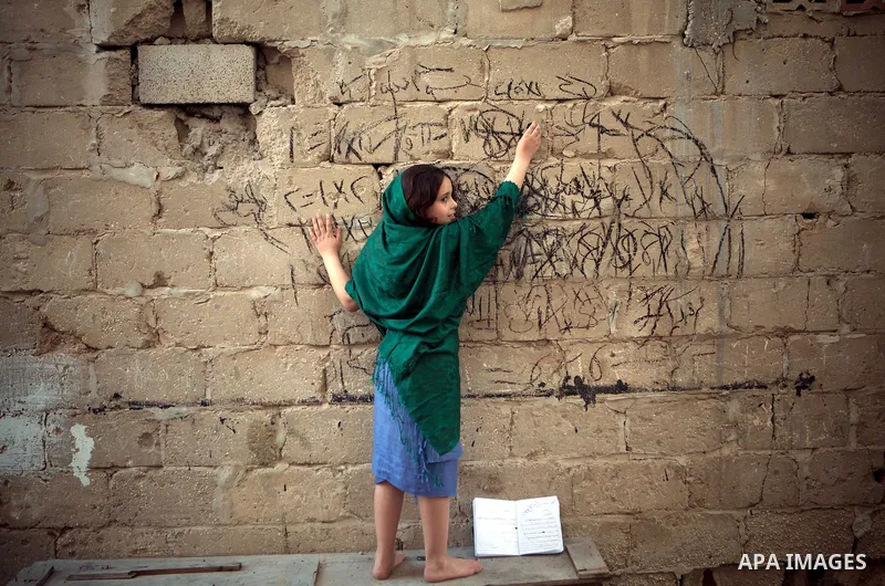 A Palestinian girl writes on a wall as she plays outside her family's house, in the east of ‎Gaza‬ City near the border with Israel, May 1, 2014. Photo by Ezz Zanoun