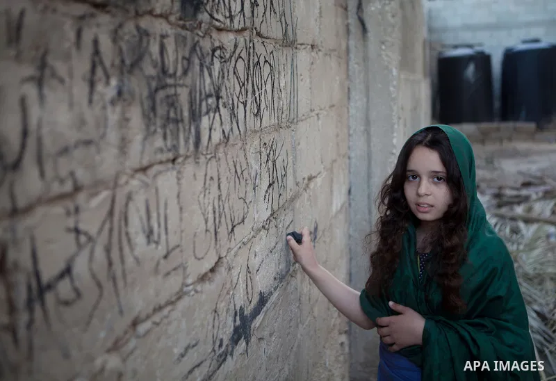 A Palestinian girl writes on a wall as she plays outside her family's house, in the east of ‎Gaza‬ City near the border with Israel, May 1, 2014. Photo by Ezz Zanoun