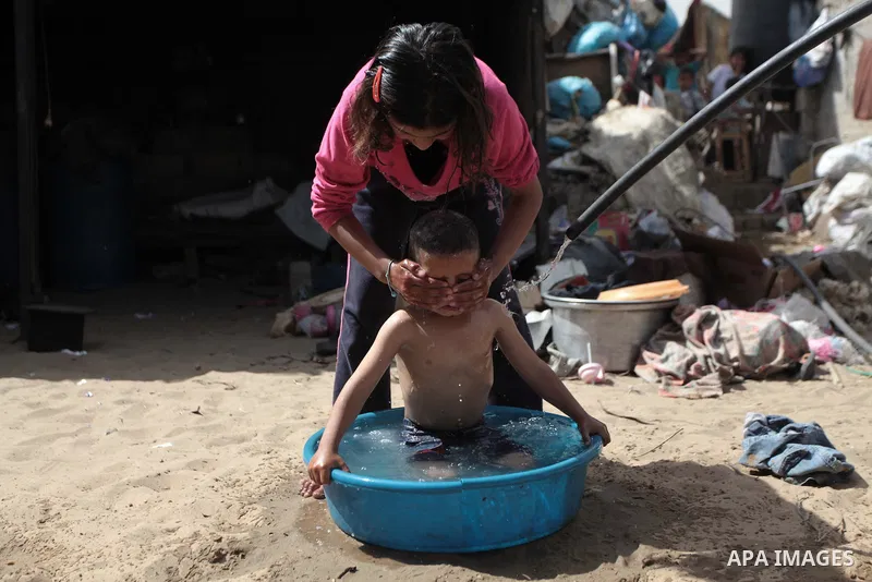 A Palestinian Bedouin girl bathes her brother outside a shed near their family's house, in Gaza City on May 04, 2014. Photo by Ashraf Amra
