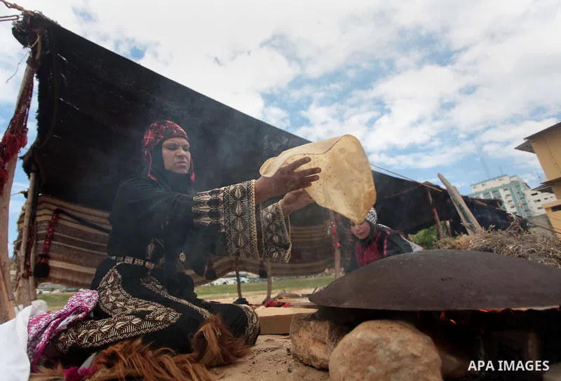 A Palestinian woman bakes bread on a typical domed metal griddle for baking traditional flat bread, known locally in the region as the saj, in Gaza city on May 12, 2014, as part of a cultural exhibition to mark the 66th...