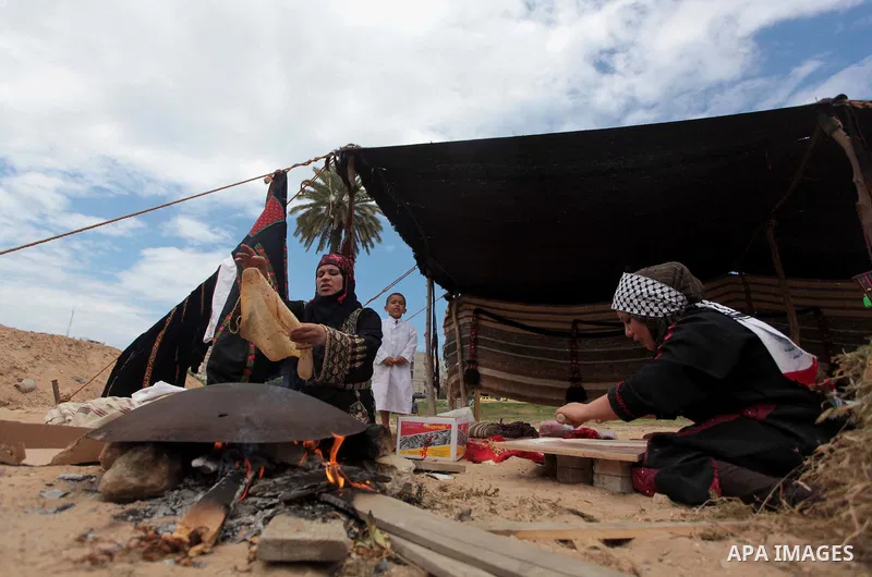 Palestinian women bake bread on a typical domed metal griddle for baking traditional flat bread, known locally in the region as the saj, in Gaza city on May 12, 2014, as part of a cultural exhibition to mark the 66th ann...
