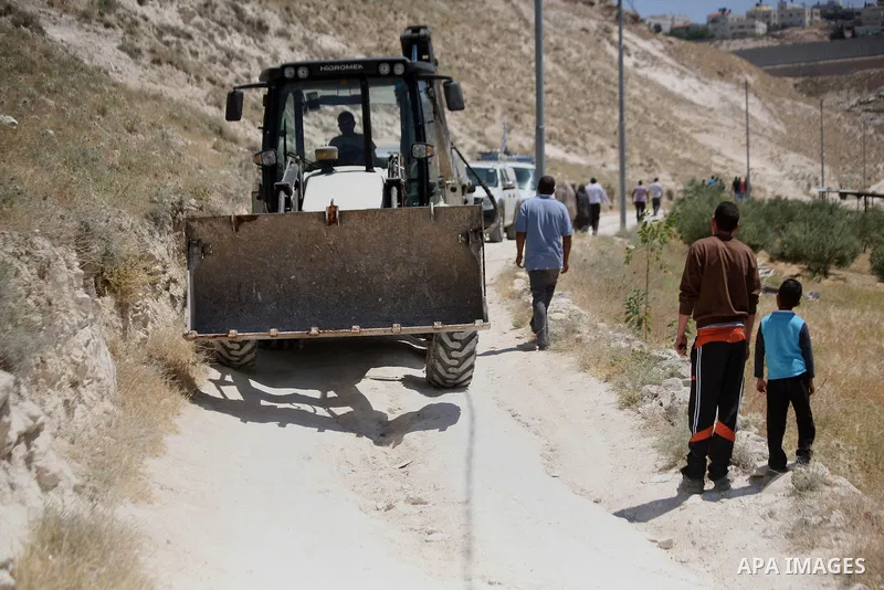 Palestinians walk past Israeli police vehicles and bulldozer after demolish their house by Israeli municipality workers under the pretext of building without permit, at Jabal al-Mukaber district, East Jerusalem May 14, 2...