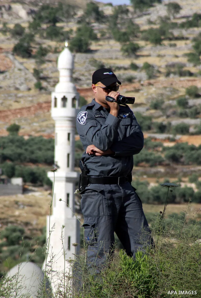 An Israeli policeman uses a video camera as Israeli army reservists take part in a demonstration against settlers' phenomenon of so-called "price tag" attacks, outside the Yitzhar Jewish settlement, near the West Bank ci...