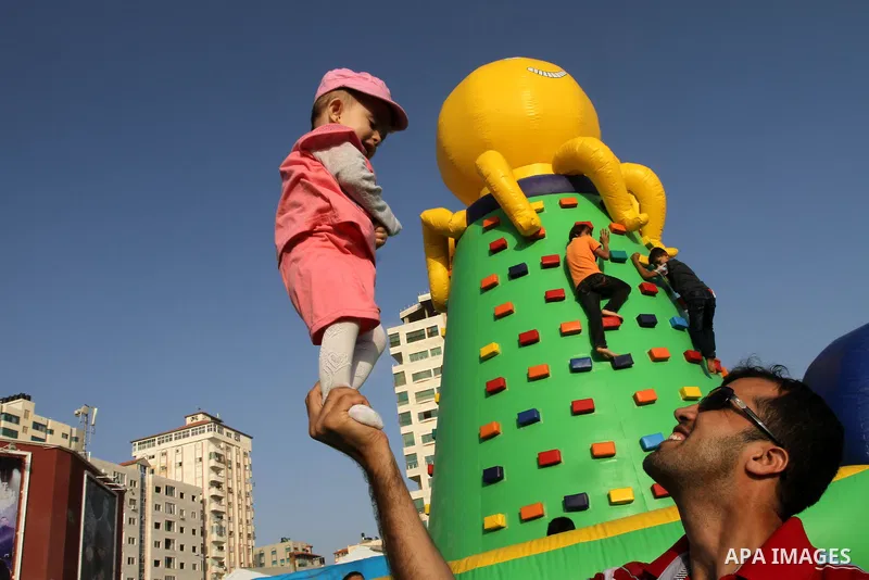 A Palestinian man carries his daughter as children play on a huge inflatable toy at Aqua Park, in Gaza City May 22, 2014. Photo by Mohammed Asad