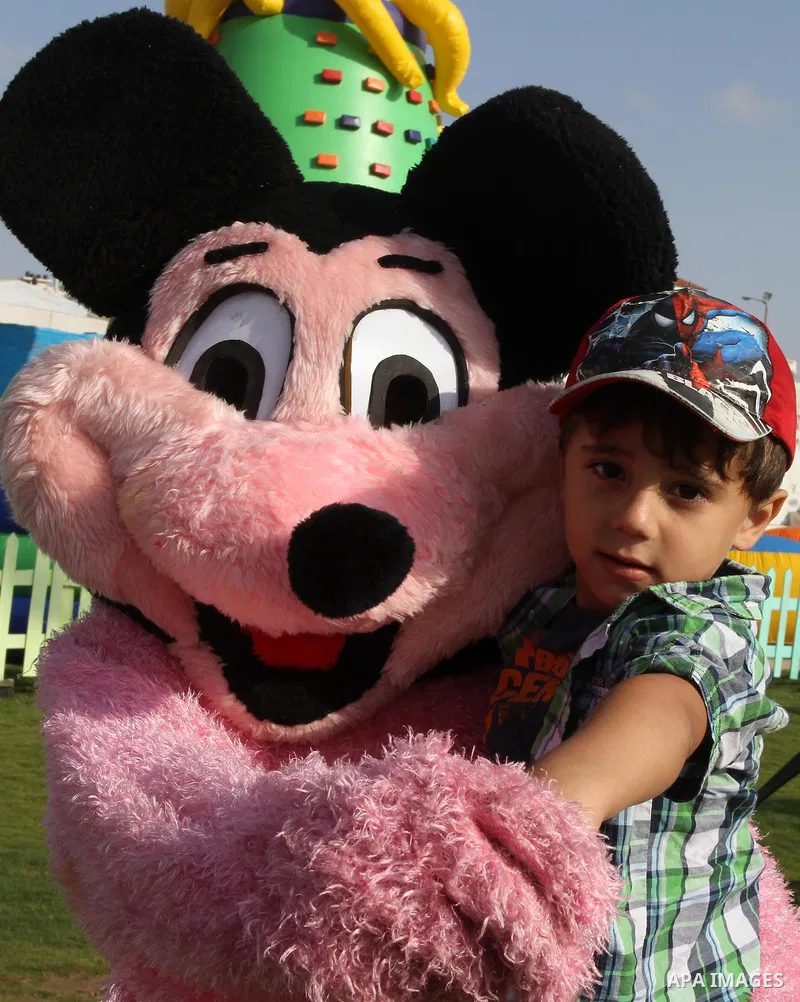 A Palestinian man wearing a mouse costume carries a boy as they play at Aqua Park, in Gaza City May 22, 2014. Photo by Mohammed Asad