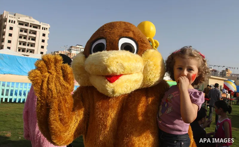 A Palestinian man wearing a bear costume carries a girl as they play at Aqua Park, in Gaza City May 22, 2014. Photo by Mohammed Asad