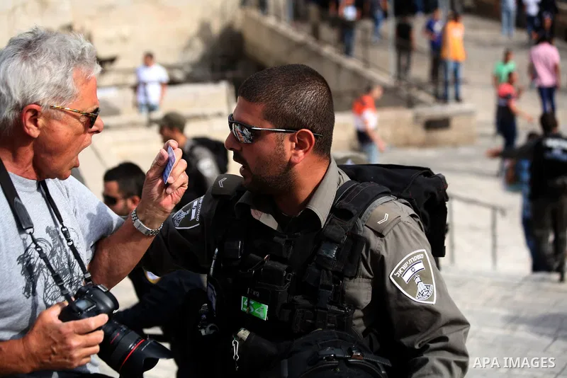 A foreign photographer shows his card to An Israel border officer as he prevent him from work as Ultra-nationalist Israelis take part in the "flag march" through Damascus Gate in east Jerusalem on May 28, 2014 celebratin...