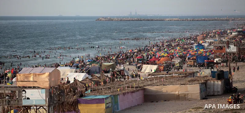 Palestinians residents swim, surf and ride a small boat in the Mediterranean Sea at sunset, in Gaza City, on May 30, 2014. Gaza residents ran to the beach to cool off during the hot weather, as high temperatures hit the...