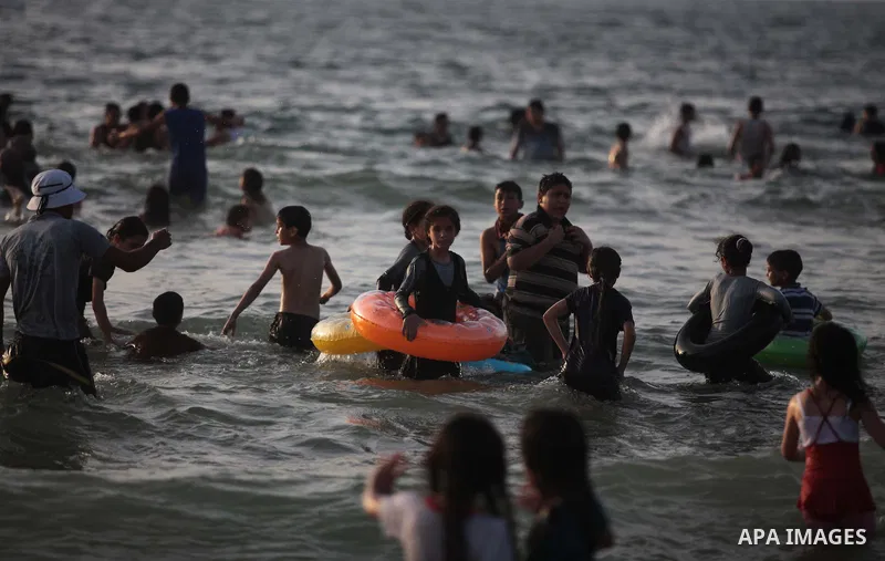 Palestinians residents swim, surf and ride a small boat in the Mediterranean Sea at sunset, in Gaza City, on May 30, 2014. Gaza residents ran to the beach to cool off during the hot weather, as high temperatures hit the...