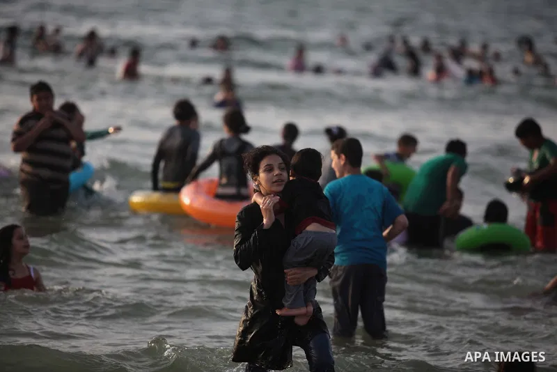 Palestinians residents swim, surf and ride a small boat in the Mediterranean Sea at sunset, in Gaza City, on May 30, 2014. Gaza residents ran to the beach to cool off during the hot weather, as high temperatures hit the...