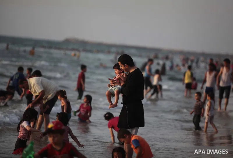 Palestinians residents swim, surf and ride a small boat in the Mediterranean Sea at sunset, in Gaza City, on May 30, 2014. Gaza residents ran to the beach to cool off during the hot weather, as high temperatures hit the...