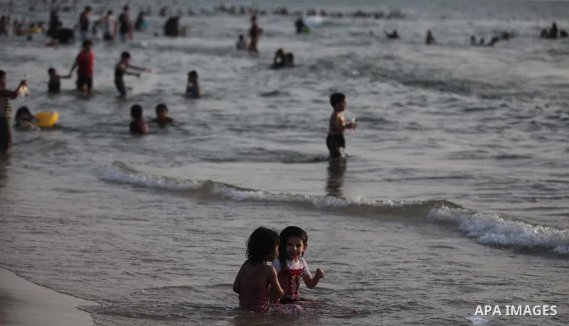 Palestinians residents swim, surf and ride a small boat in the Mediterranean Sea at sunset, in Gaza City, on May 30, 2014. Gaza residents ran to the beach to cool off during the hot weather, as high temperatures hit the...