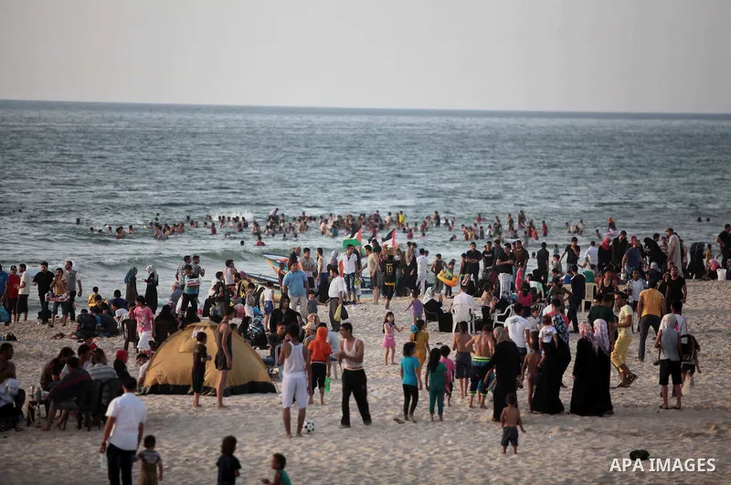 Palestinians residents swim, surf and ride a small boat in the Mediterranean Sea at sunset, in Gaza City, on May 30, 2014. Gaza residents ran to the beach to cool off during the hot weather, as high temperatures hit the...