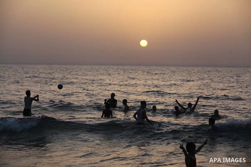 Palestinians residents swim, surf and ride a small boat in the Mediterranean Sea at sunset, in Gaza City, on May 30, 2014. Gaza residents ran to the beach to cool off during the hot weather, as high temperatures hit the...