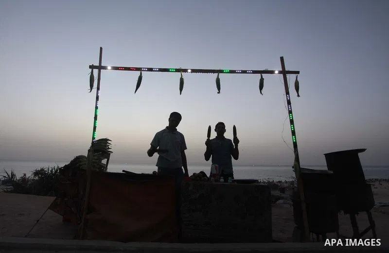 Palestinian men sell grilled corns on a beach, in Gaza City, on May 30, 2014. Gaza residents ran to the beach to cool off during the hot weather, as high temperatures hit the city Photo by Ashraf Amra