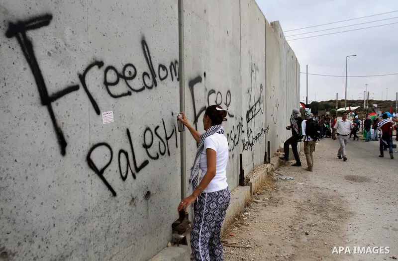 A Palestinian protester sprays a slogan reading in Arabic 'Free Prisoners' on a concrete segment of a separation wall in the West Bank city of Tulkarem, 31 May 2014. Reportedly dozens of Palestinians were injured during...
