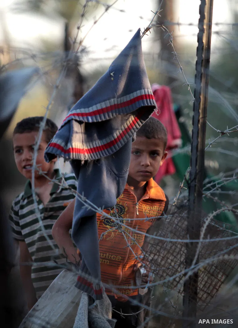 A photo taken on May 26, 2014, shows Palestinian children watch their relatives through a fence as they play football outside their homes, in Deir al-Balah in the central of Gaza Strip. Palestinians share a billion or mo...