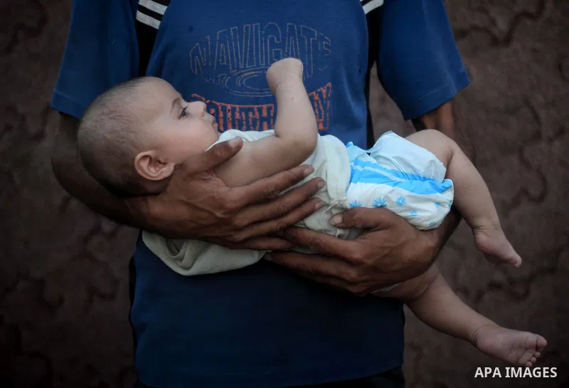 A Palestinian boy carries his bother's outside their house at Al-Zaitoun neighborhood in the central Gaza Strip, on June 02, 2014. Photo by Ezz al-Zanoun