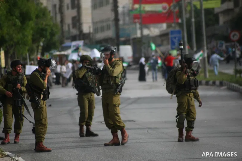 Israeli soldiers stand guard as Palestinians hold national flags and posters of jailed relatives during a protest in solidarity with prisoners on hunger strike,in the West Bank city of Hebron June 4, 2014. Some 120 Pales...