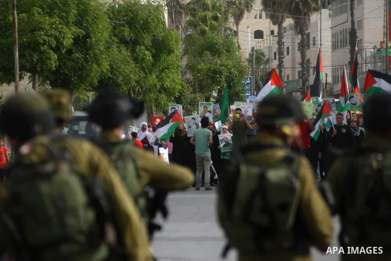 Israeli soldiers stand guard as Palestinians hold national flags and posters of jailed relatives during a protest in solidarity with prisoners on hunger strike,in the West Bank city of Hebron June 4, 2014. Some 120 Pales...