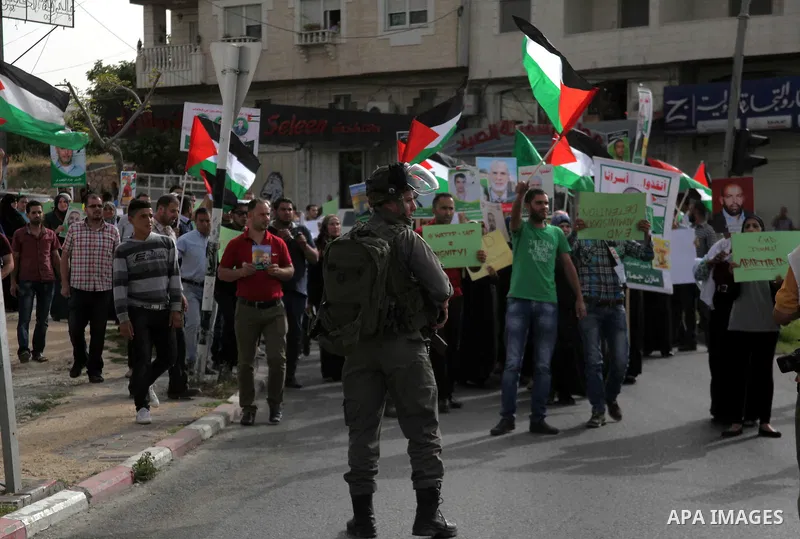 Israeli soldiers stand guard as Palestinians hold national flags and posters of jailed relatives during a protest in solidarity with prisoners on hunger strike,in the West Bank city of Hebron June 4, 2014. Some 120 Pales...
