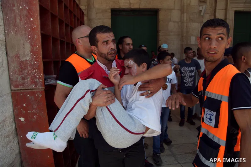 A Palestinian medic man carries a boy suffering from pepper sprayed on his face by Israeli riot police during clashes following Friday prayers at the al-Aqsa mosque compound in Jerusalem's Old City on June 13, 2014. Phot...