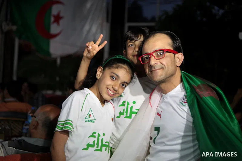 A Palestinian man with his kids wear the Algerian football team costume and as they watch the match between Algeria and Belgium during the 2014 FIFA World Cup in Brazil, on June 17, 2014 in a cafe in Gaza City. Photo by...