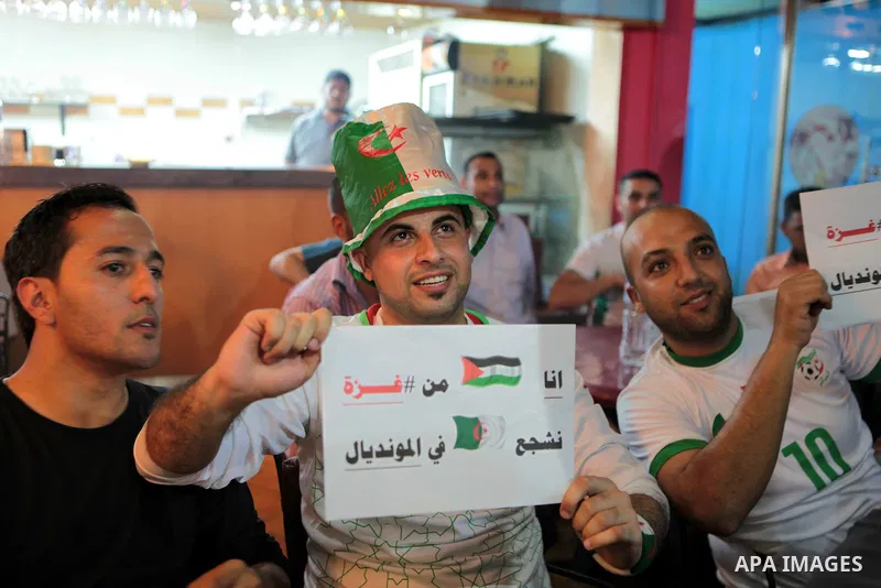 Palestinians wear the Algerian football team costume and hold placards as they watch the match between Algeria and Belgium during the 2014 FIFA World Cup in Brazil, on June 17, 2014 at a cafe in Gaza City. Photo by Ezz Z...