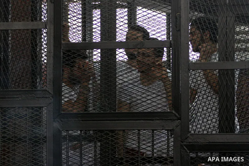 Al-Jazeera journalists stand inside court's cage as their wait to listen the ruling at a court in Cairo June 23, 2014. Three Al Jazeera journalists were jailed for seven years in Egypt on Monday after a court convicted t...