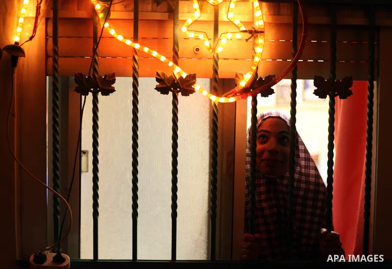A Palestinian girl looks through a window decorated with lights in the old city of Jerusalem on June 26, 2014, as people prepare for the upcoming Muslim holy fasting month of Ramadan. Muslims around the world celebrate R...