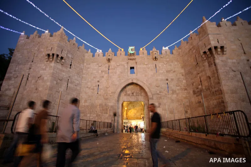 People walk under lights decorating Damascus Gate outside the old city of Jerusalem on June 26, 2014, as Muslims prepare for the upcoming holy fasting month of Ramadan. Muslims around the world celebrate Ramadan, the hol...