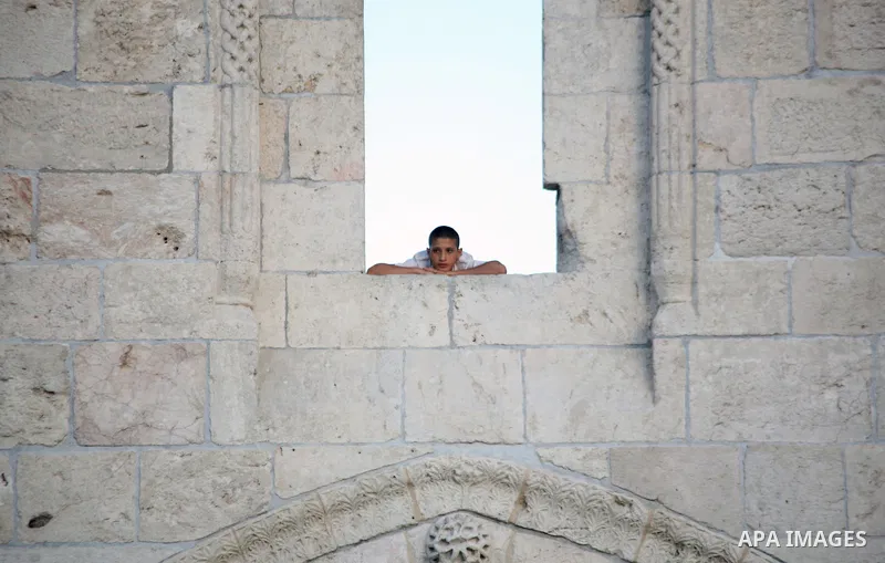 A Palestinian youth looks from a window on the Damascus Gate in the old city of Jerusalem on June 26, 2014, as Muslims prepare for the upcoming holy fasting month of Ramadan. Muslims around the world celebrate Ramadan, t...