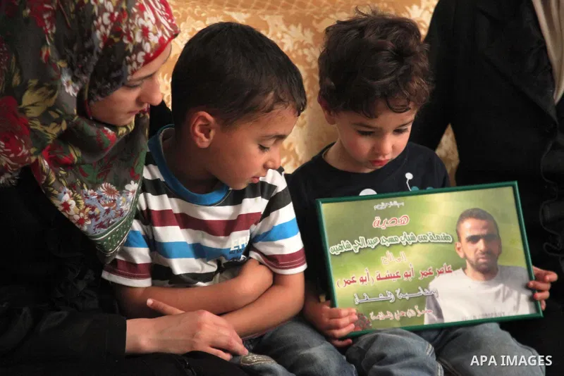 The son of Amer Abu Aysha holds his father's picture as he poses with his brother and his mother for media in their house in the West Bank city of Hebron June 27, 2014. Israel on Thursday named Abu Aysha as one of two le...