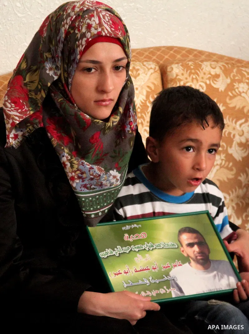 The son of Amer Abu Aysha holds his father's picture as he poses with his mother for media in their house in the West Bank city of Hebron June 27, 2014. Israel on Thursday named Abu Aysha as one of two leading suspects f...