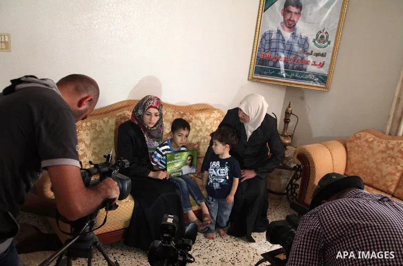 The son of Amer Abu Aysha holds his father's picture as he poses with his grandmother (R), his brother and his mother for media in their house in the West Bank city of Hebron June 27, 2014. Israel on Thursday named Abu A...