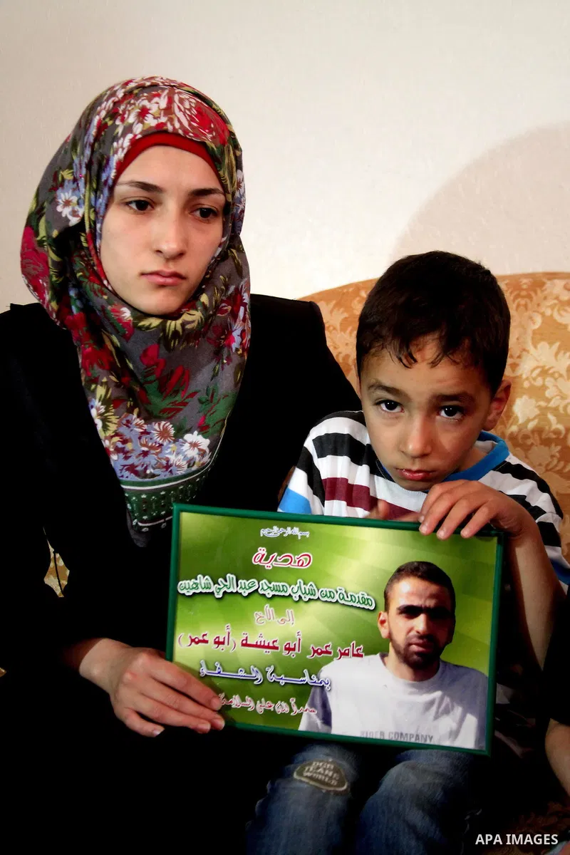 The son of Amer Abu Aysha holds his father's picture as he poses with his mother for media in their house in the West Bank city of Hebron June 27, 2014. Israel on Thursday named Abu Aysha as one of two leading suspects f...