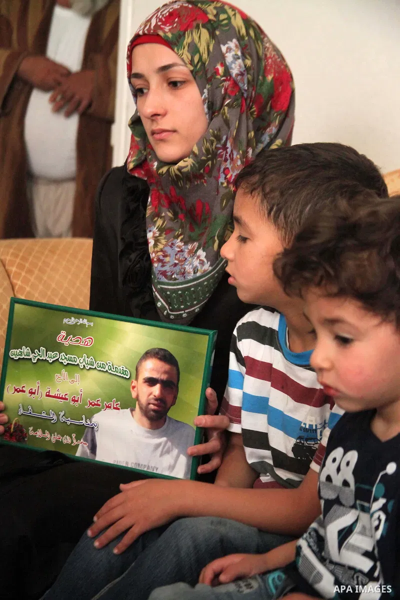 The son of Amer Abu Aysha holds his father's picture as he poses with his brother and his mother for media in their house in the West Bank city of Hebron June 27, 2014. Israel on Thursday named Abu Aysha as one of two le...