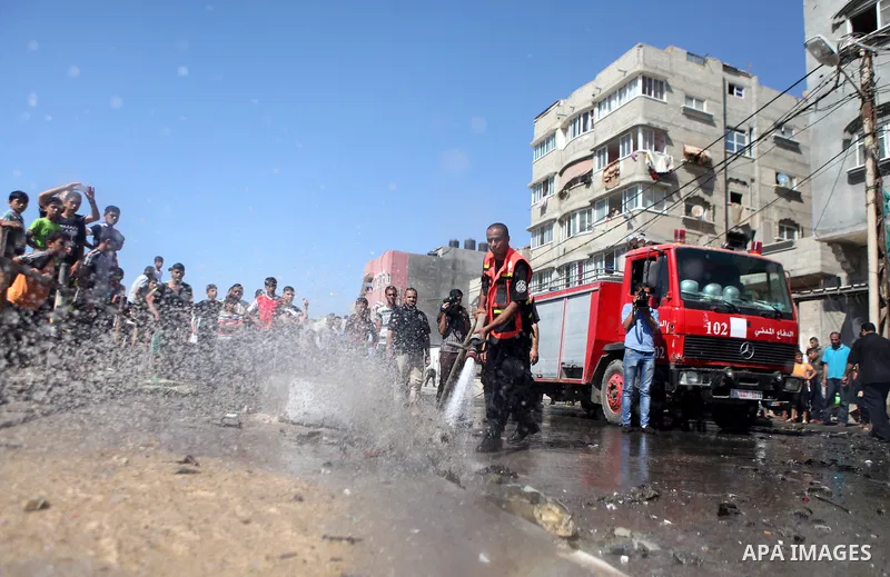 Firefighters wash the debris of a car that was targeted by an Israeli air strike in Gaza City on June 27, 2014. The air strike killed two Palestinians, medics said, hours after a bomb exploded near troops manning Israel'...