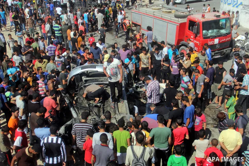 Palestinians gather around a car that was targeted by an Israeli air strike in Gaza City on June 27, 2014. The air strike killed two Palestinians, medics said, hours after a bomb exploded near troops manning Israel's sec...