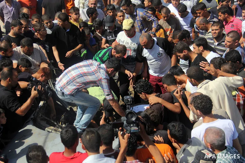 Palestinians gather around a car that was targeted by an Israeli air strike in Gaza City on June 27, 2014. The air strike killed two Palestinians, medics said, hours after a bomb exploded near troops manning Israel's sec...