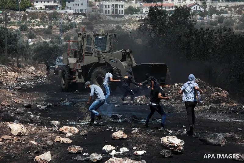Palestinian protester throw stones towards an Israeli military bulldozer during clashes following a weekly protest against the expropriation of Palestinian land by Israel in the West Bank village of Kfar Qaddum, near Nab...
