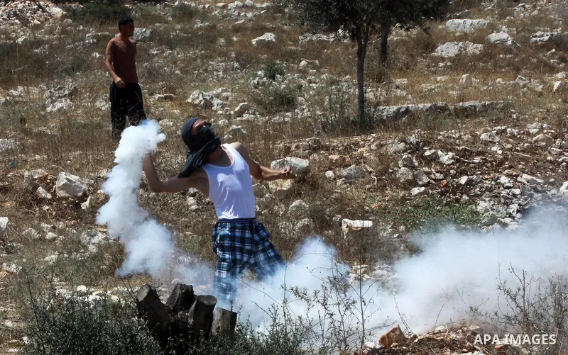 A Palestinian protester throws back a tear gas canister towards Israeli security forces during clashes following a weekly protest against the expropriation of Palestinian land by Israel in the West Bank village of Kfar Q...